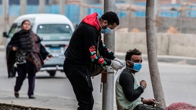 An volunteer ties a mask onto an Egyptian man in a street in Cairo. AFP