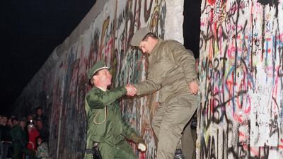 West German policeman, left, gives a helping hand to an East German border guard who climbs through a gap of the Berlin Wall when East Germany opened another passage at Potsdamer Platz in Berlin. AP Photo