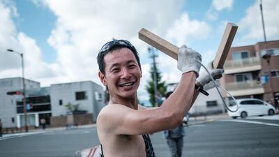 A man hitting wood pieces together to create a rhythm as participants carry a large fireworks cylinder. AFP
