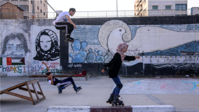 Teens rollerblading on a rooftop in Gaza with murals as a backdrop. Photo by Samar Abu Elouf