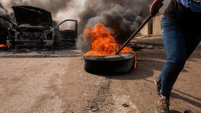 An Iraqi demonstrator moves a burning tyre next to the smoking remains of an Iraqi anti-riot vehicle during a demonstration in the southern city of Basra on Sunday. AFP