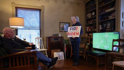 A woman holds a campaign sign while her husband watches an American football game, as they prepare to hold a caucus at their home in Silver City, Iowa. Reuters