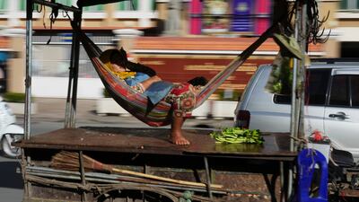 A Cambodian vendor sleeps in a hammock being carried by a motor-cart past the Phnom Penh Municipal Court building in Phnom Penh, Cambodia. AP