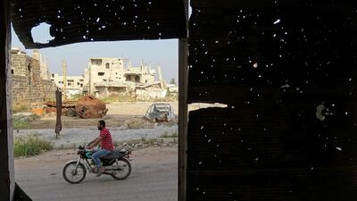 A picture taken through a metal venetian blind with bullets holes shows a man riding his motorbike in a rebel-held area of Daraa, in southern Syria. Mahmoud Irshaidat / AFP