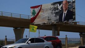 A Hezbollah flag waves from a car in Sidon, Lebanon, as it passes a billboard showing President Joseph Aoun and a slogan promoting diplomacy ‘to end war in Lebanon'. AFP