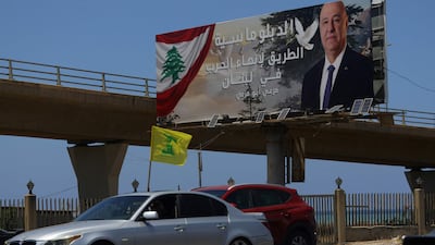 A Hezbollah flag waves from a car in Sidon, Lebanon, as it passes a billboard showing President Joseph Aoun and a slogan promoting diplomacy ‘to end war in Lebanon'. AFP