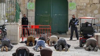 This picture taken on March 23, 2020 shows Palestinian Muslim men prostrate in prayer as Israeli security forces watch near the closed gate of the Aqsa mosque compound, which was closed by the Jordan Waqf religious authority administering the site as part of preventive measures against the spread of the COVID-19 novel coronavirus, in Jerusalem. / AFP / Ahmad GHARABLI