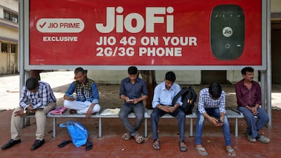 Commuters use their mobile phones as they wait at a bus stop with an advertisement of Reliance Industries' Jio telecoms unit, in Mumbai, India. The firm's new device has shaken up the domestic market. REUTERS/Shailesh Andrade/File Photo