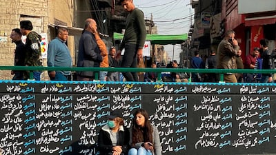 Women sit by a wall with names of anti-government protesters who have been killed in demonstrations in Tahrir Square during ongoing protests in Baghdad, Iraq. AP
