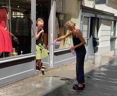 Fashion designer Beatrice Ferrant, centre, and a neighbour throw water on the street to tackle rising temperatures. Sunniva Rose / The National