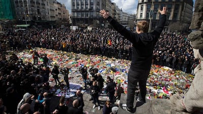 A man gestures as masked and hooded men arrive at a square outside the stock exchange in Brussels on March 27, 2016. Kristof van Accom / Belga / AFP