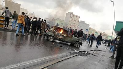 Iranian protesters gather around a burning car in Tehran. AFP