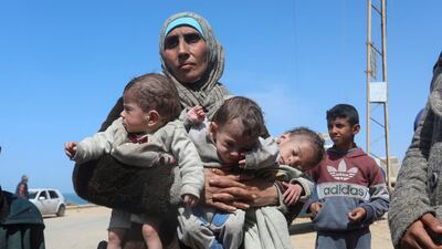 A Palestinian woman fleeing the Israeli raid at Al Shifa Hospital carries her triplet children as she heads south. Reuters