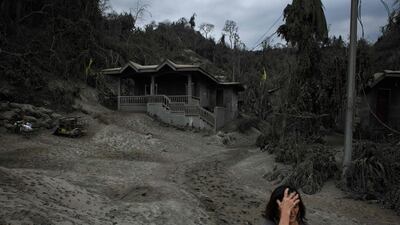 Andalida Cabono stands before her home covered in ash from the eruption of the Taal volcano, as she prepares to leave for an evacuation centre on January 17. AFP