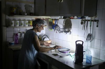 Samira Hanna, 70, washes dishes in her kitchen as she uses a portable electric light due to a power cut, in Beirut, Lebanon July 6. Reuters