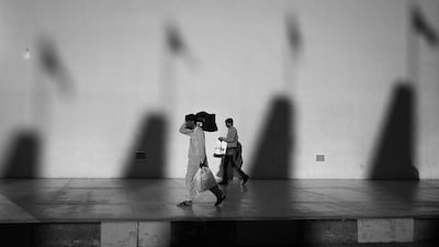 Two men make their way along the side of the Abu Dhabi Taxi and Bus Terminal in the shadows of Al Nahyan Stadium. Brian Kerrigan / The National