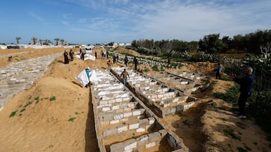 People walk next to bodies placed in graves during a mass burial of unidentified Palestinians, whose bodies were released after being held in Israel during the war, in Deir Al-Balah. Reuters