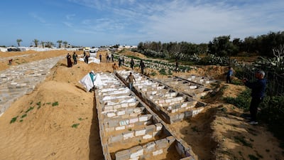 People walk next to bodies placed in graves during a mass burial of unidentified Palestinians, whose bodies were released after being held in Israel during the war, in Deir Al-Balah. Reuters