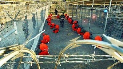 Detainees in orange jumpsuits sit in a holding area under the surveillance of US military police at Camp X-Ray at the US naval base, Guantanamo Bay, Cuba, during processing in 2002.
