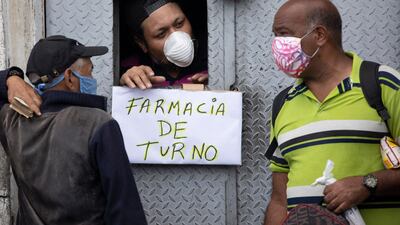 A man attends customers through an opening from which hangs a handwritten sign that reads in Spanish: "Pharmacy on duty," in Caracas, Venezuela. AP Photo