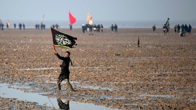 A Shiite Muslim pilgrim waves a flag as he walks in mud near the Gulf waters at the start of his march from Iraq's southern city of Al Faw towards Karbala.