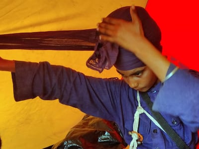 Fatesh Singh, 14, ties his turban. The teenager joined the Nihang warrior community four months ago and has since been stationed at Singhu border, near New Delhi, to support protesting farmers. Taniya Dutta for The National