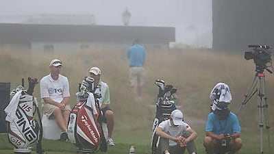 Noh Seung-yul, second right, of South Korea sits next to his bag on the practice range during another fog delay today.