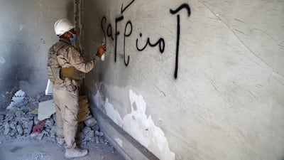 A member of a demining squad writes the word 'safe' on a wall.