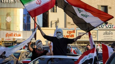 A man waves the flags of Iraq and Iran from the sunroof of a car during recent ceasefire celebrations in Baghdad. AFP