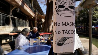 A sign requiring masks is seen near diners eating at a restaurant on the River Walk on March 3, 2021, in San Antonio, Texas. AP