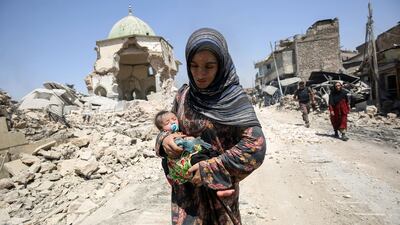 An Iraqi woman, carrying an infant, walks by the destroyed Al-Nuri Mosque as she flees from the Old City of Mosul on July 5, 2017. AFP