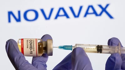 FILE PHOTO: A woman holds a small bottle labelled with a "Coronavirus COVID-19 Vaccine" sticker and a medical syringe in front of displayed Novavax logo in this illustration. Reuters