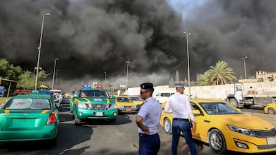Iraqi traffic policemen stand outside the country's biggest ballot warehouse, where votes for the eastern Baghdad district were stored, as a column of black smoke billows from a the building, in the capital Baghdad. Sabah Arar / AFP