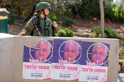 An Israeli soldier stands next to posters of Palestinian Authority President Mahmoud Abbas with a slogan reading: "Eliminate the people sponsoring murder", in the occupied West Bank. AFP