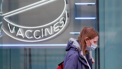 A woman wearing a mask against coronavirus walks past a neon sign display at the Wellcome Institute in London. AP