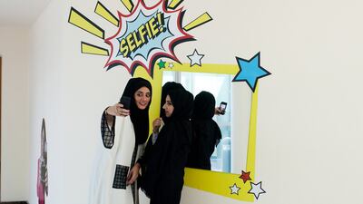 Two young ladies take selfies in the hallway.