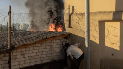 A man takes shelter as smoke and flames rise from garages damaged by Russian missile and drone attacks on Kyiv. AFP