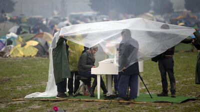 Syrian pianist Nour Alkhzam, center left, plays the piano as Chinese dissident artist Ai WeiWei, center right, holds a plastic sheet, along with other people, during a heavy rain at the northern Greek border station of Idomeni on March 12, 2016. Vadim Ghirda/AP Photo