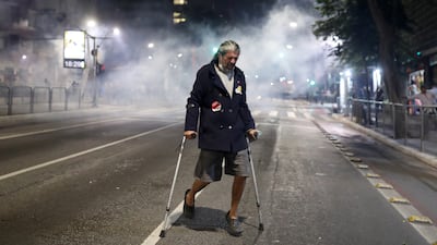 A man on crutches moves away from tear gas thrown by police during a protest in Sao Paulo to demand the impeachment of Brazil's President Jair Bolsonaro and against his handling of the pandemic.