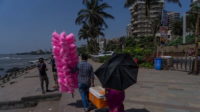 A man selling candy floss in Mumbai helps a water vendor who is using an umbrella as a parasol. AP