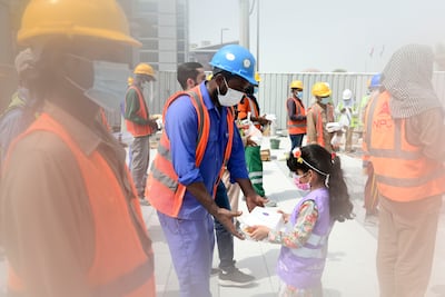 A young volunteer hands out food to construction workers in Abu Dhabi. Khushnum Bhandari / The National