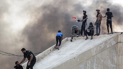 Protesters stand on a concrete arch connected to a burning building between the capital Baghdad's Tahrir Square and the high-security Green Zone district. AFP
