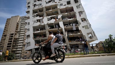 Two people ride a motorcycle past a heavily damaged apartment building in Catia La Mar. AFP