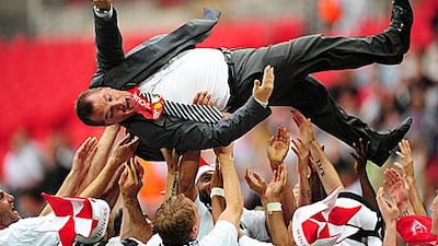 Swansea City players celebrate promotion by throwing their manager Brendan Rodgers into the air.