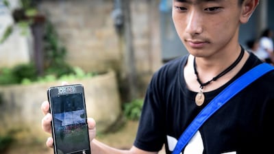 Thananchai Saengtan, 15, shows the camera a photo of his missing friends, at a football pitch near Tham Luang cave. Lillian Suwanrumpha / AFP