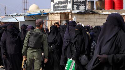 A members of the Syrian Kurdish internal security forces walks past women and children queueing at Al Hol camp in north-east Syria. AFP