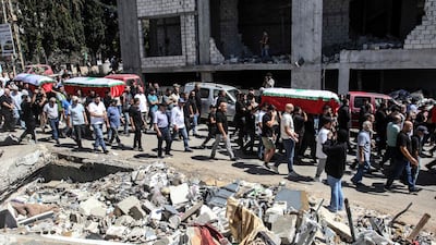 Lebanese mourners carry coffins past the debris of buildings destroyed in a deadly Israeli air strike on the village of Kfar Remman. AFP