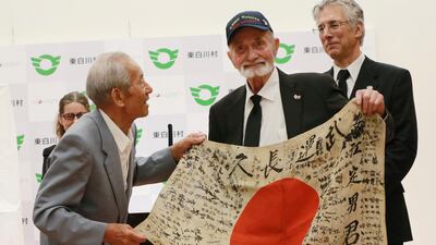 American Second World War veteran Marvin Strombo, second right, and Tatsuya Yasue, left, hold the Japanese flag with autographed messages which Mr Strombo took from the body of Japanese soldier Sadao Yasue, who was killed in the Pacific in 1944. The emotional handover took place at a ceremony in Higashishirakawa, in central Japan's Gifu prefecture on Tuesday, August 15, 2017. Eugene Hoshiko / AP