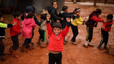 A child poses as others behind him walk in a line through the mud at a flooded camp for displaced Syrians near the village of Killi in the north of the northwestern Idlib province. AFP