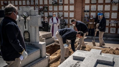 A priest and relatives pray as a victim of the Covid-19 is buried by undertakers at the Almudena cemetery in Madrid, Spain. AP